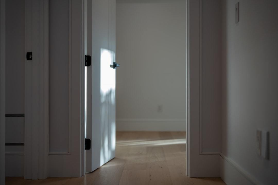 A partially open white door casting a shadow on light wooden flooring