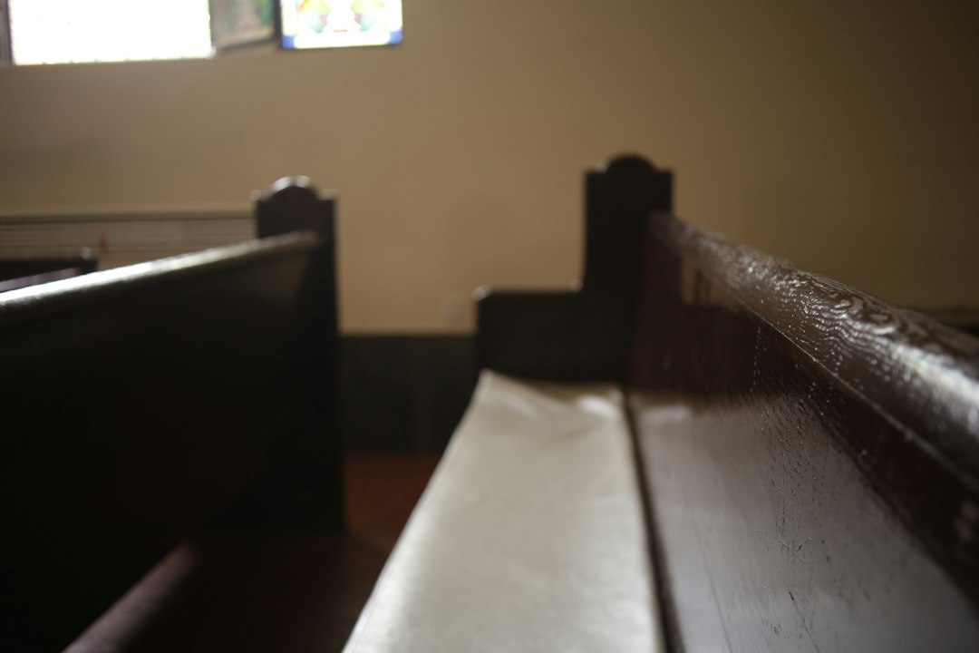 Dark wooden pews in a sunlit church interior with a stained glass window